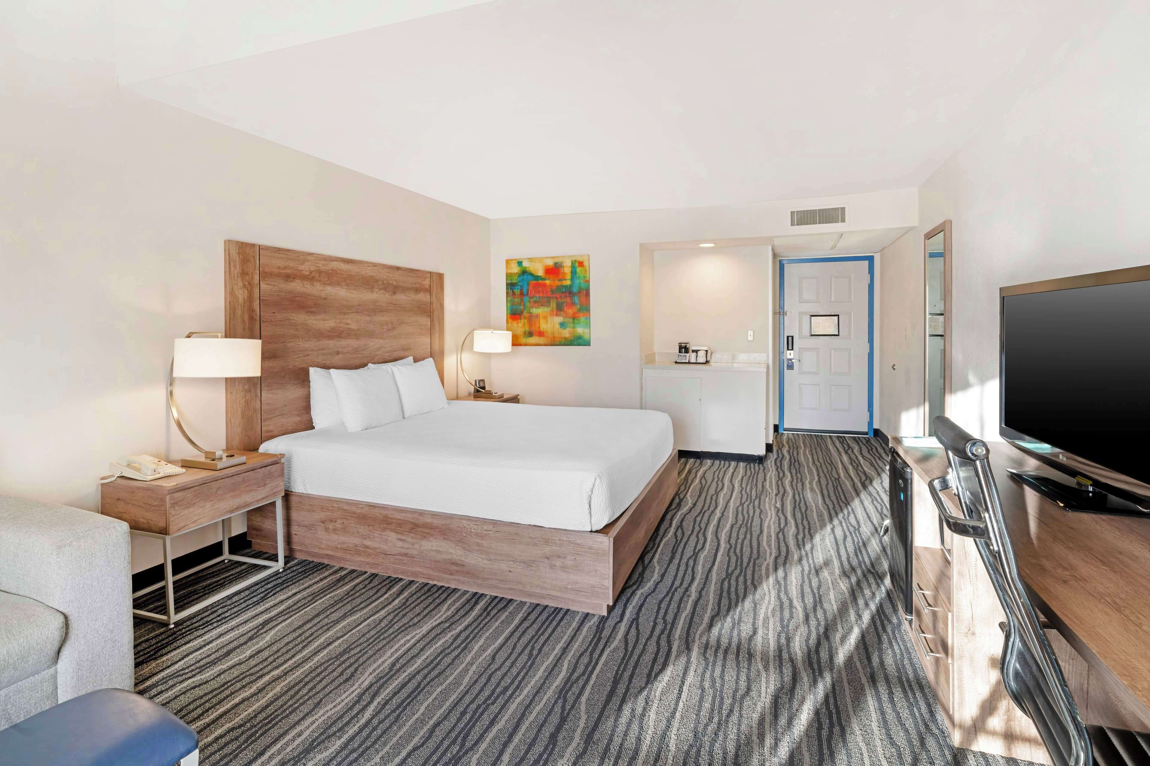 A hotel room with a bed, bedside tables, a desk with a TV, and a bathroom door.