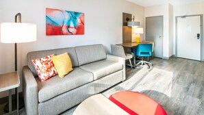 Ein modernes Hotelzimmer mit einer grauen Couch, einem Schreibtisch und einem leuchtend roten Sessel.