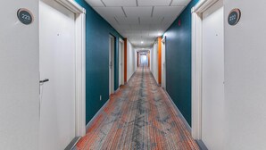 Un pasillo de hotel con puertas numeradas 223 y 222, alfombrado con un diseño estampado y paredes blancas con detalles en color aguamarina.