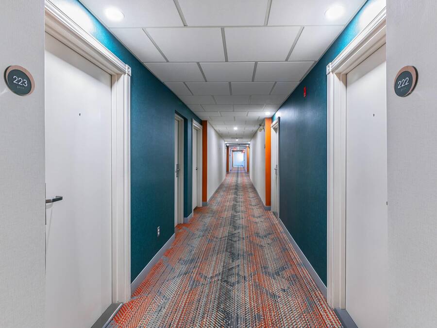 A hotel corridor with doors numbered 223 and 222, carpeted with a patterned design, and white walls with teal accents.