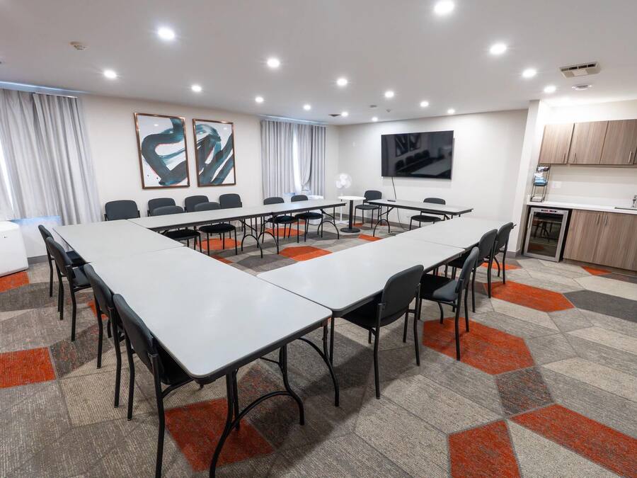 A conference room with a long table, chairs, a TV, and a kitchenette.