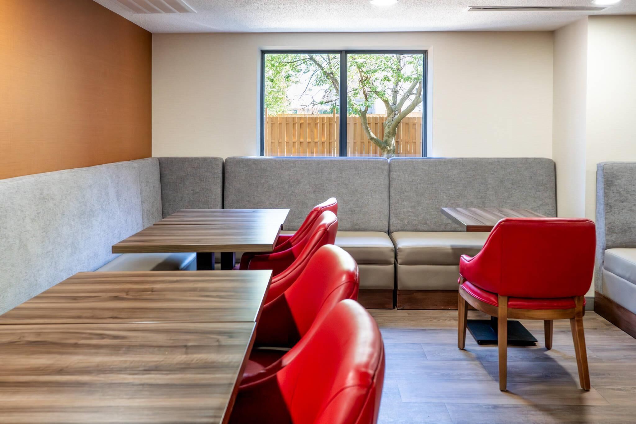 A dining area with a long wooden table, red cushioned booths, and a grey cushioned bench.