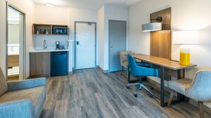 Una habitación de hotel moderna con kitchenette, una zona de comedor con una mesa y sillas, y un sofá.
