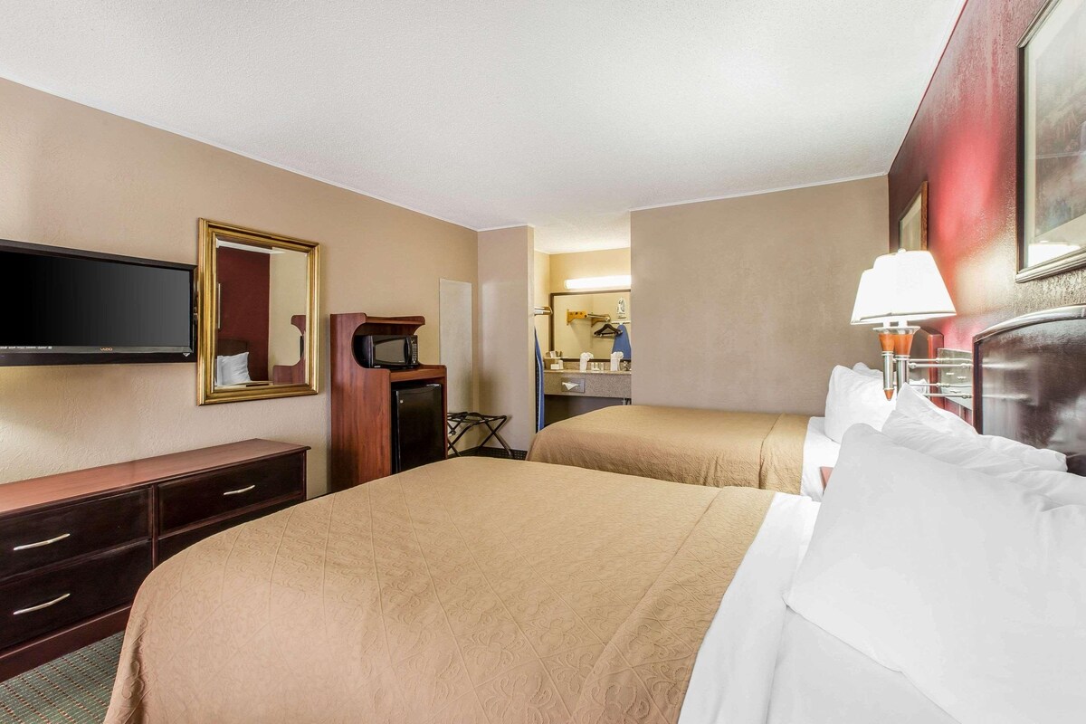 A hotel room with two beds, a TV, a desk, and a mirror.