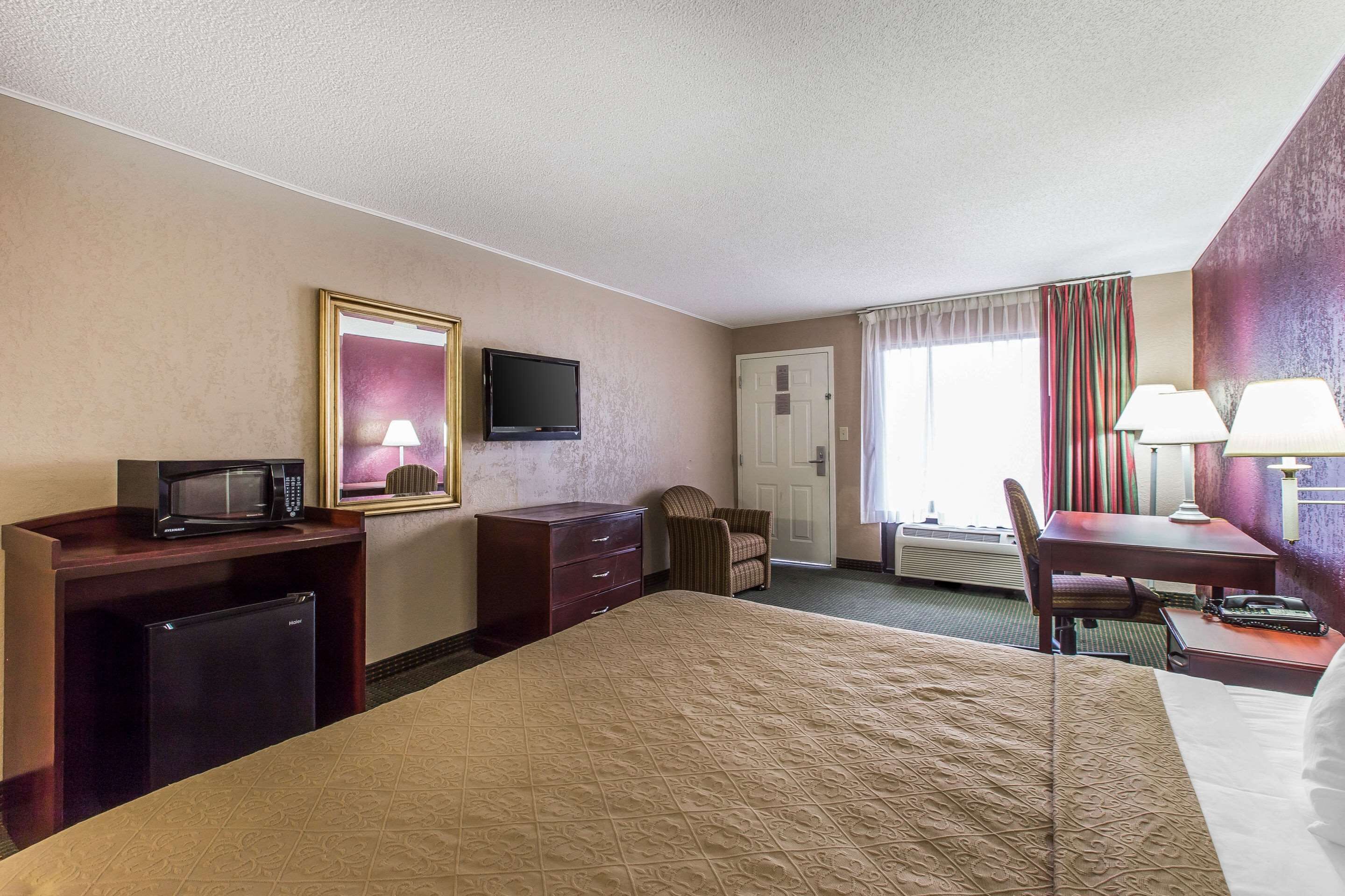 A hotel room with a bed, a desk, a chair, a television, a microwave, and a dresser.