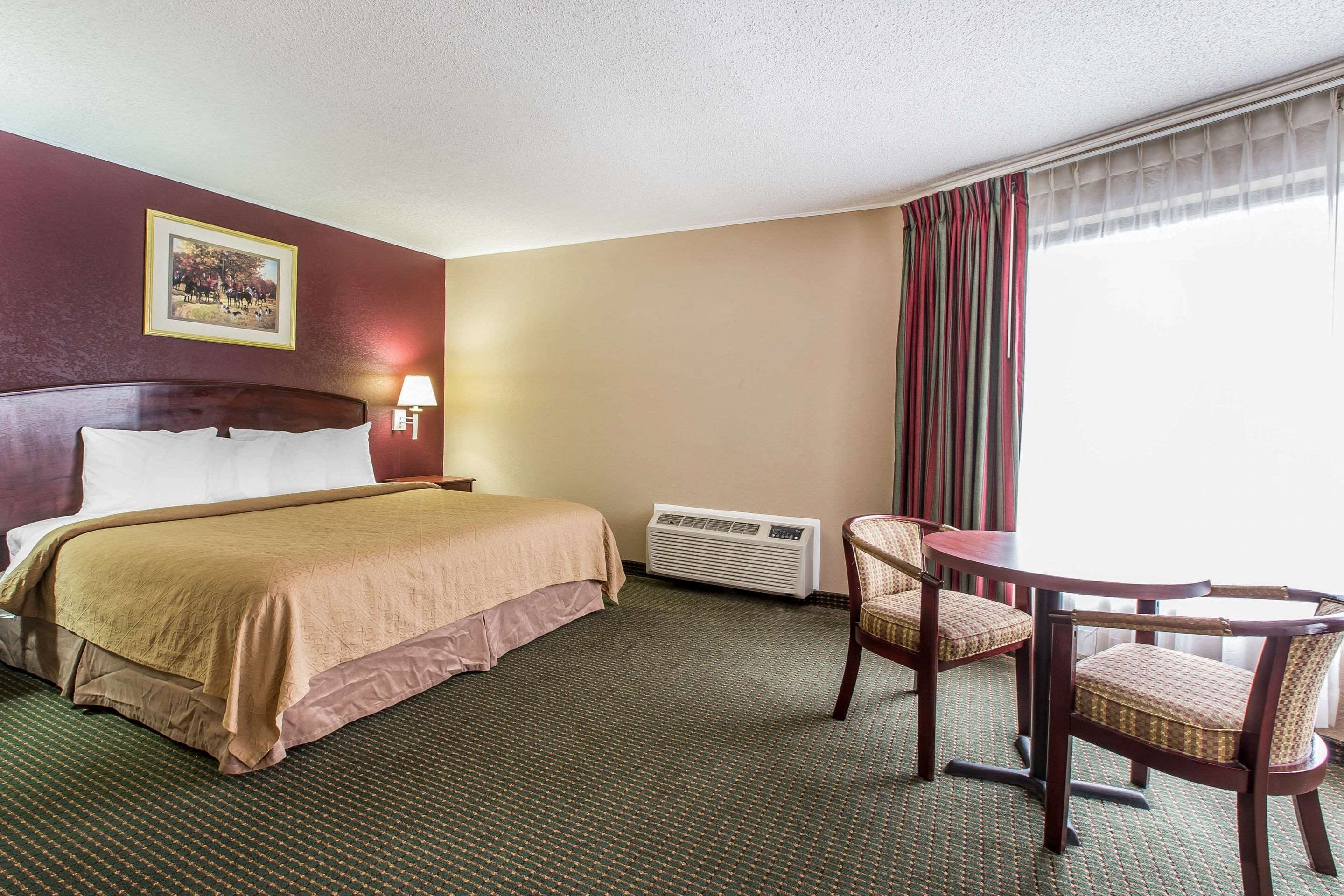A hotel room with a bed, a desk, two chairs, a lamp, and a picture on the wall.
