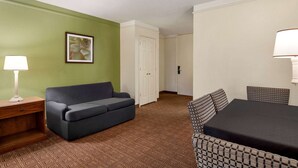A room with a green wall, a grey sofa, a patterned armchair, a small wooden nightstand, a table with a black tablecloth, and a white door.