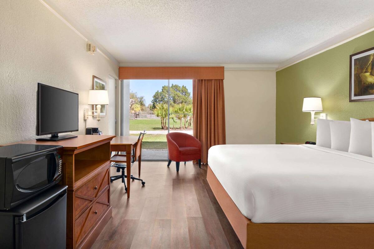 A hotel room with a bed, a desk with a television, a chair, and a view of the outdoors.