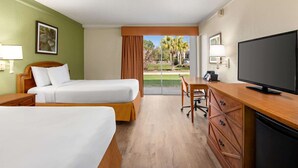 A hotel room with two beds, a desk, a television, and a view of the outdoors.
