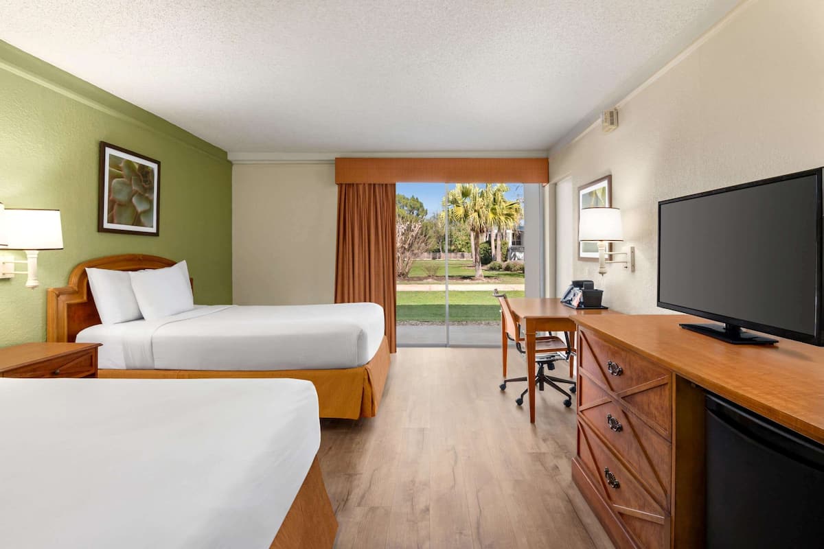 A hotel room with two beds, a desk, a television, and a view of the outdoors.