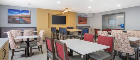Een restaurant met meerdere tafels en stoelen, een grote flatscreen televisie aan de muur en een raam met uitzicht op de omgeving.