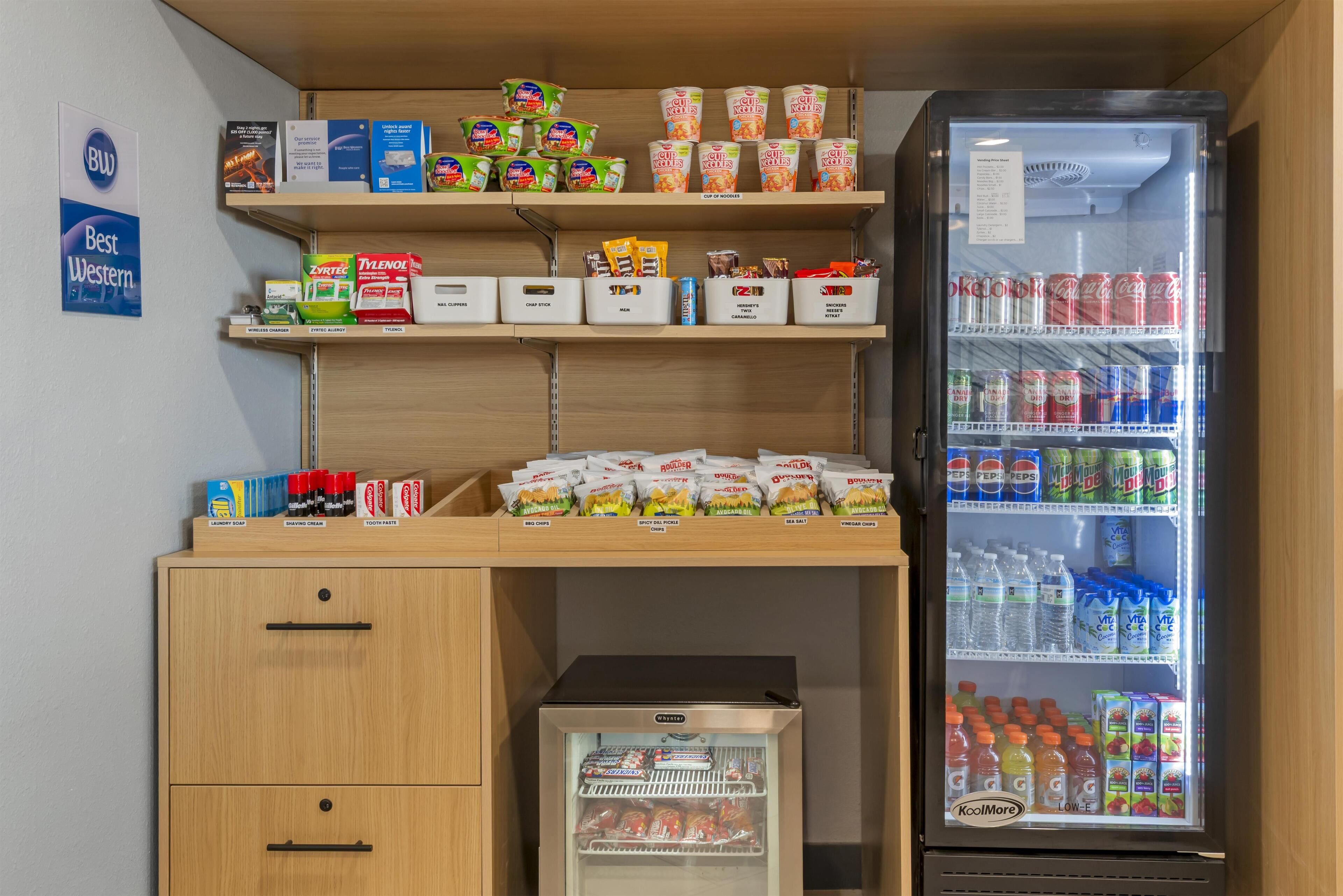 A kitchenette with a refrigerator stocked with beverages, a shelf with packaged food, and a small freezer.