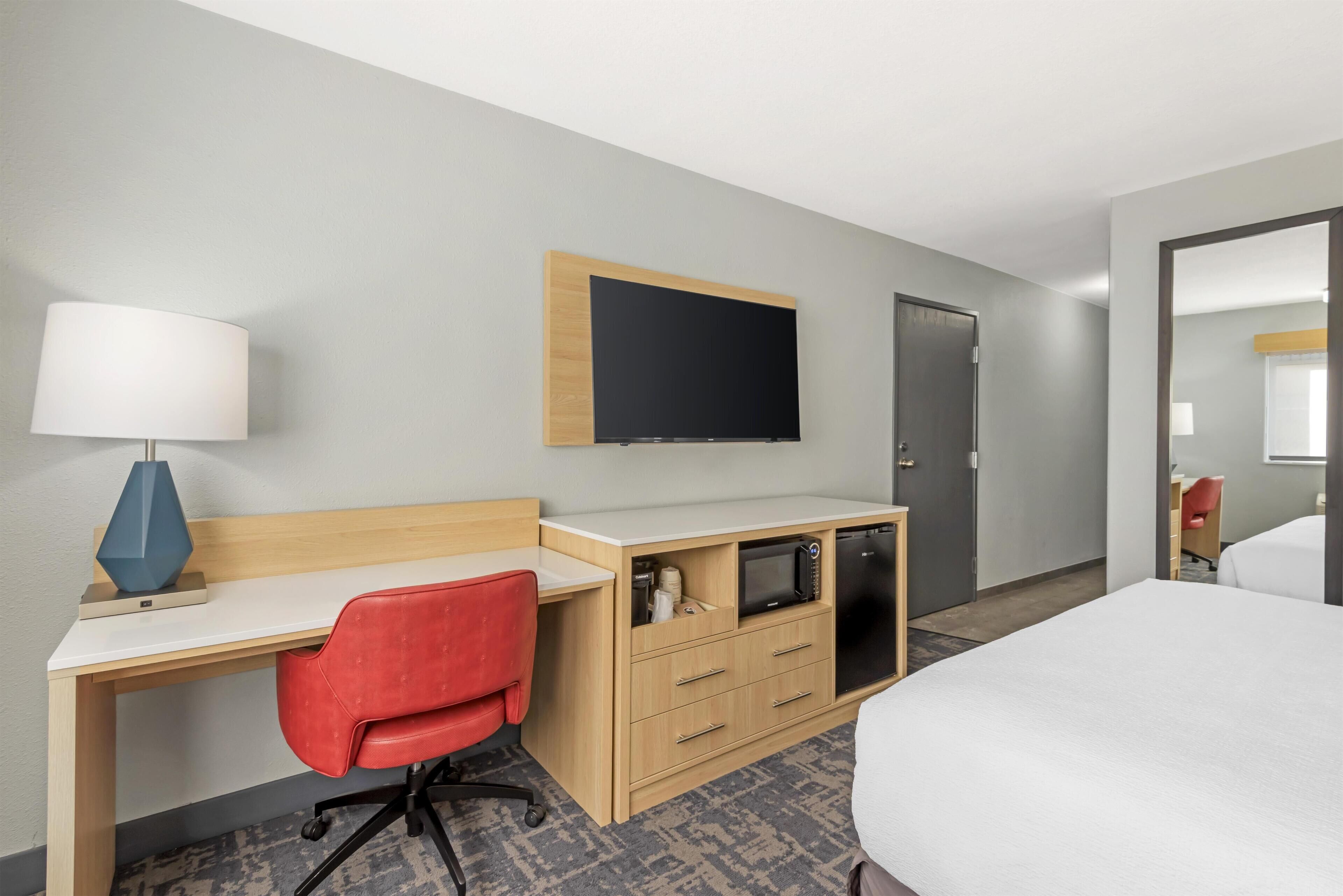 Habitación de hotel con cama, escritorio con lámpara, televisor, microondas y armario.