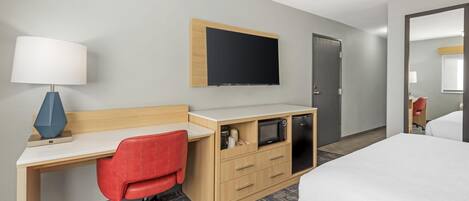 A hotel room with a bed, a desk with a lamp, a TV, a microwave, and a wardrobe.
