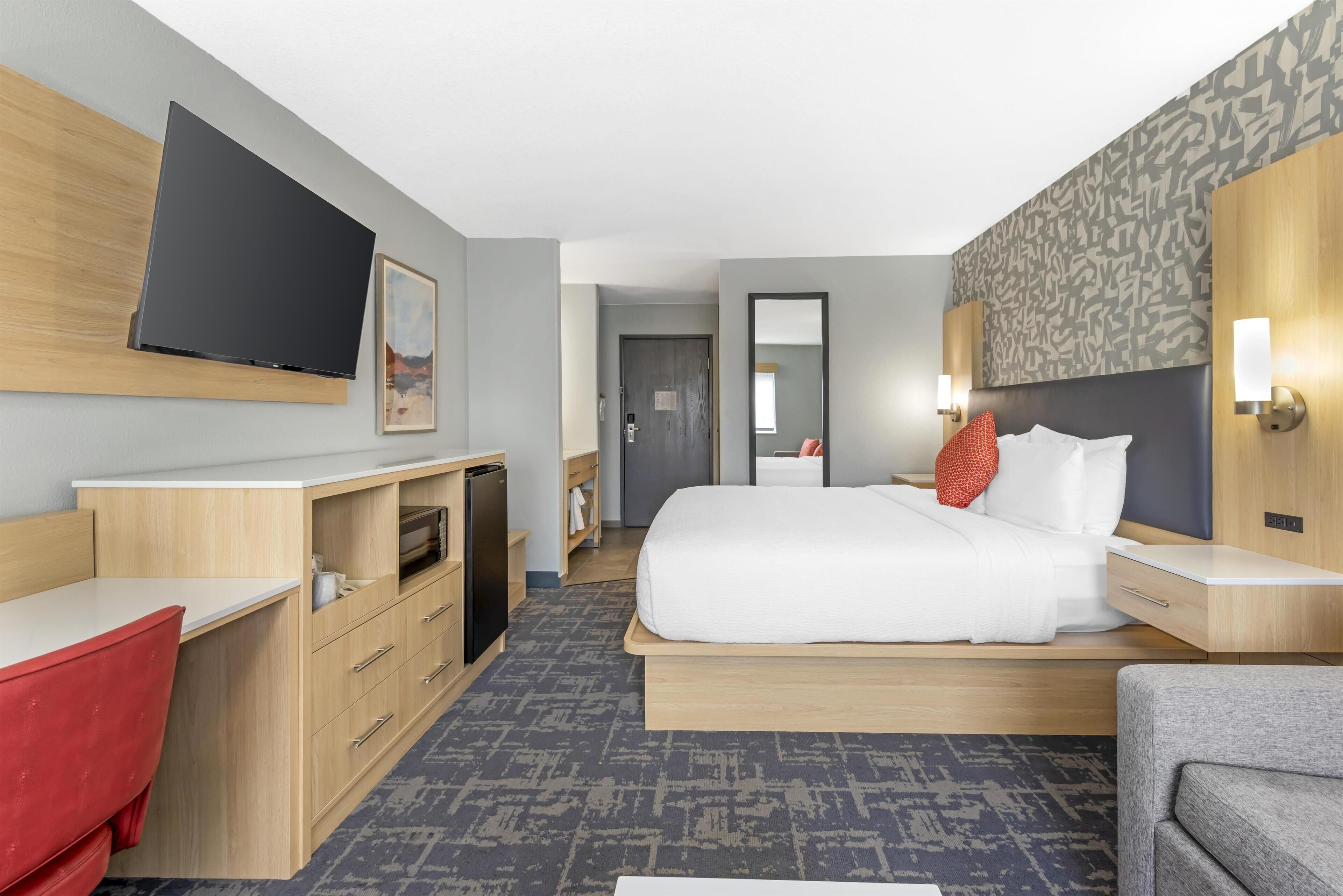 A hotel room with a bed, a desk, a TV, and a mirror.