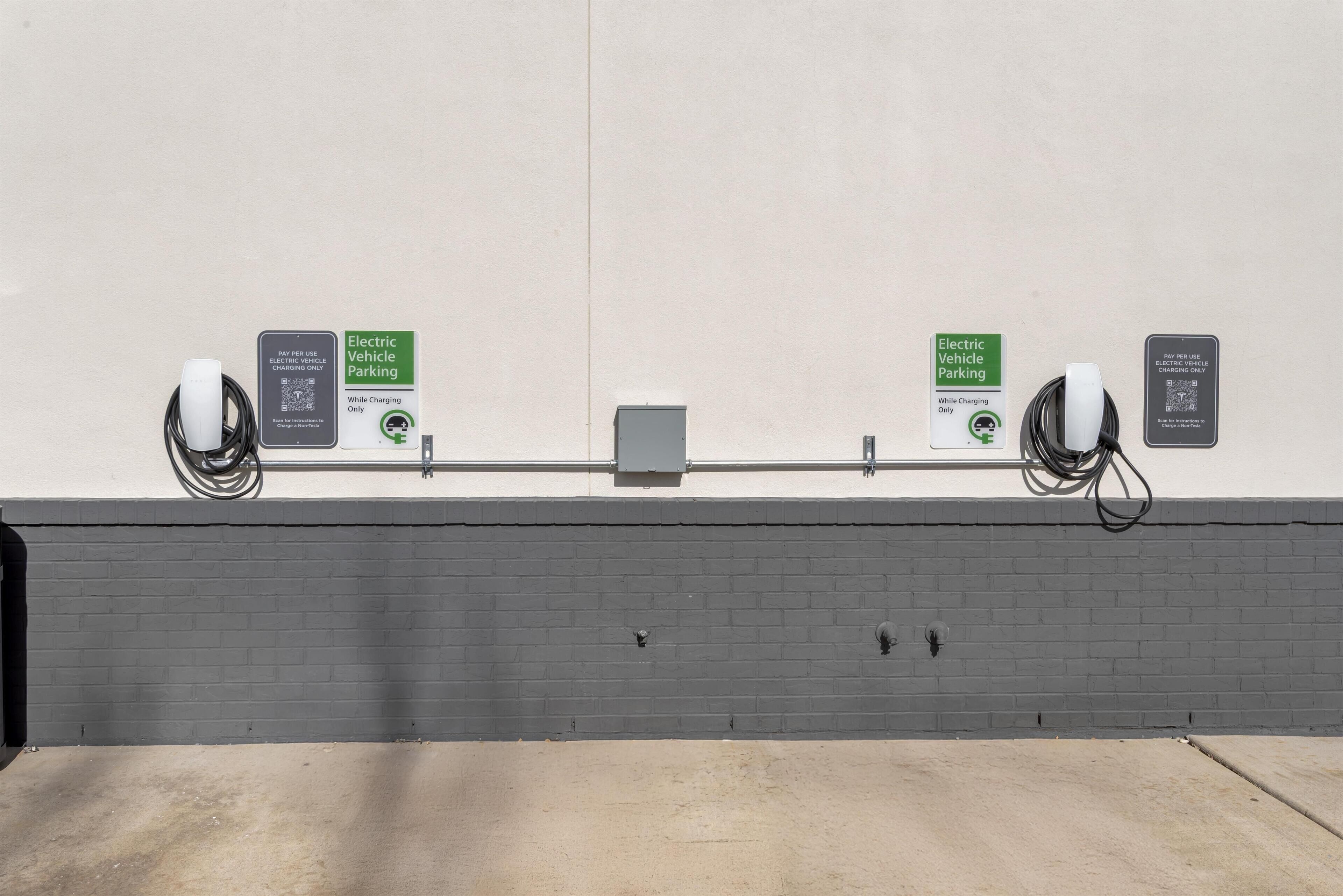 A parking area with electric vehicle charging stations, each marked with a sign indicating 'Electric Vehicle Parking' and 'While Charging Only'.