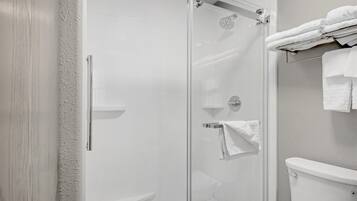 A modern bathroom with a glass-enclosed shower, a white toilet, and a towel rack with folded towels.