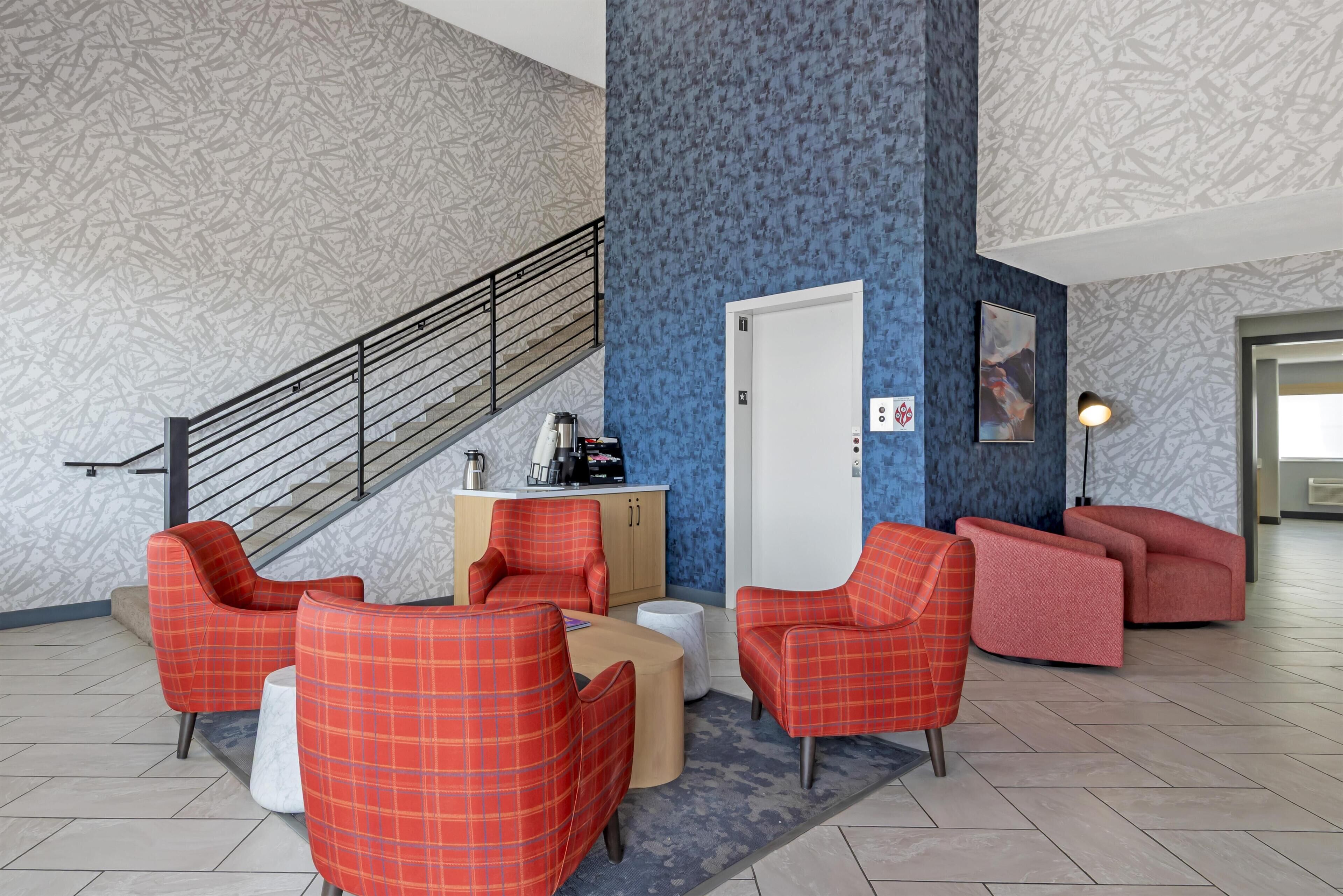 A lobby with red plaid chairs, a coffee station, and a staircase.