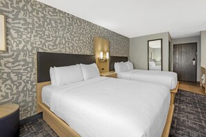 A hotel room with two beds, a patterned wall, a mirror, and a door.