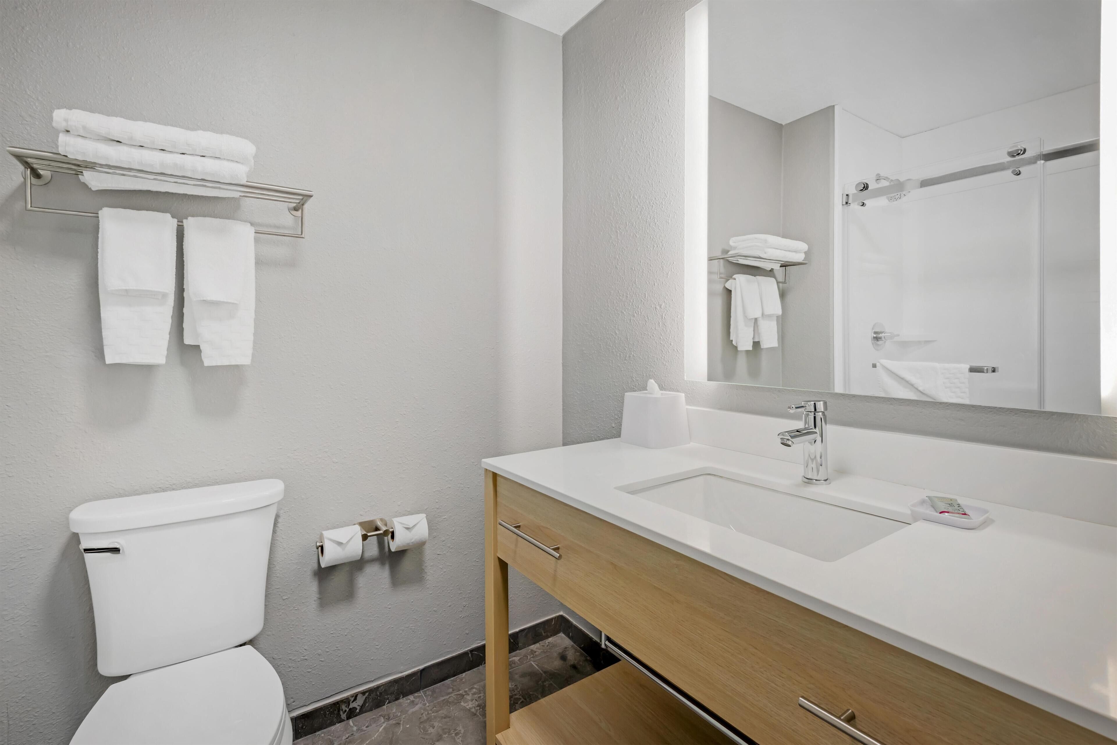 A modern bathroom with a white toilet, a sink with a mirror, and a towel rack with folded towels.