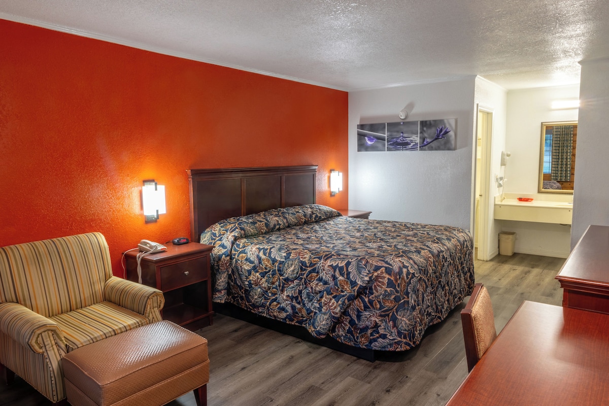 A hotel room with a bed, a chair, a nightstand, and a wall-mounted phone.