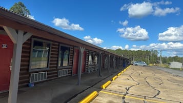 A row of log cabin-style rooms with large windows, a covered outdoor area, and a parking lot with yellow curbs.