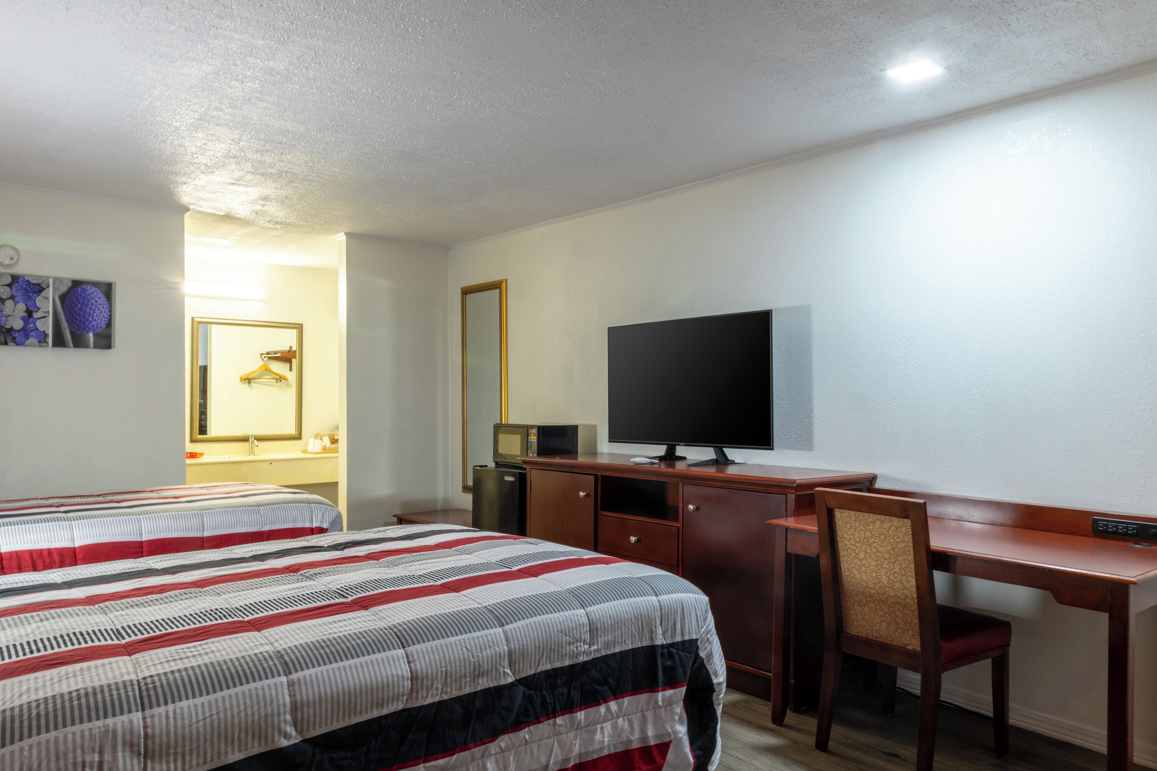 Een hotelkamer met twee bedden, een bureau met een televisie, een stoel en een spiegel.
