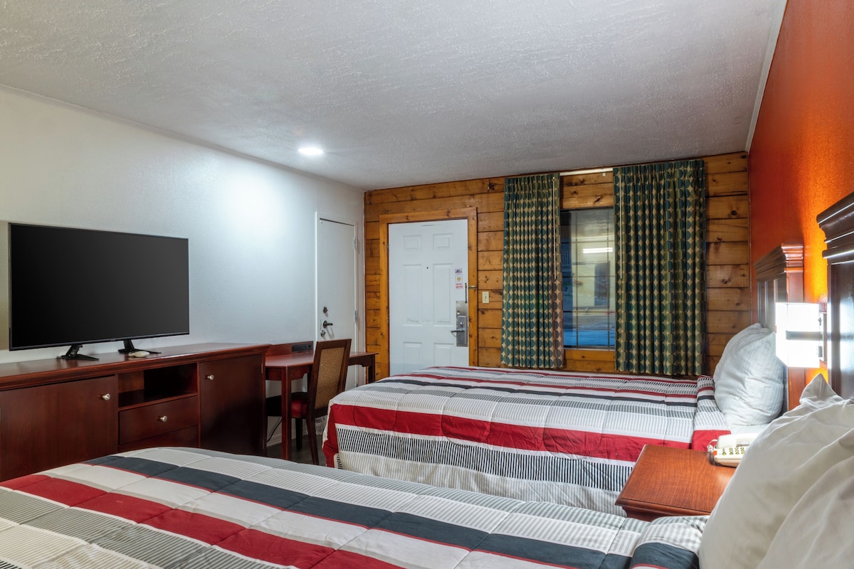 A hotel room with two beds, a desk, a television, and a window with curtains.