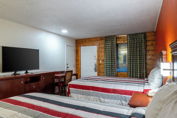 A hotel room with two beds, a desk, a television, and a window with curtains.