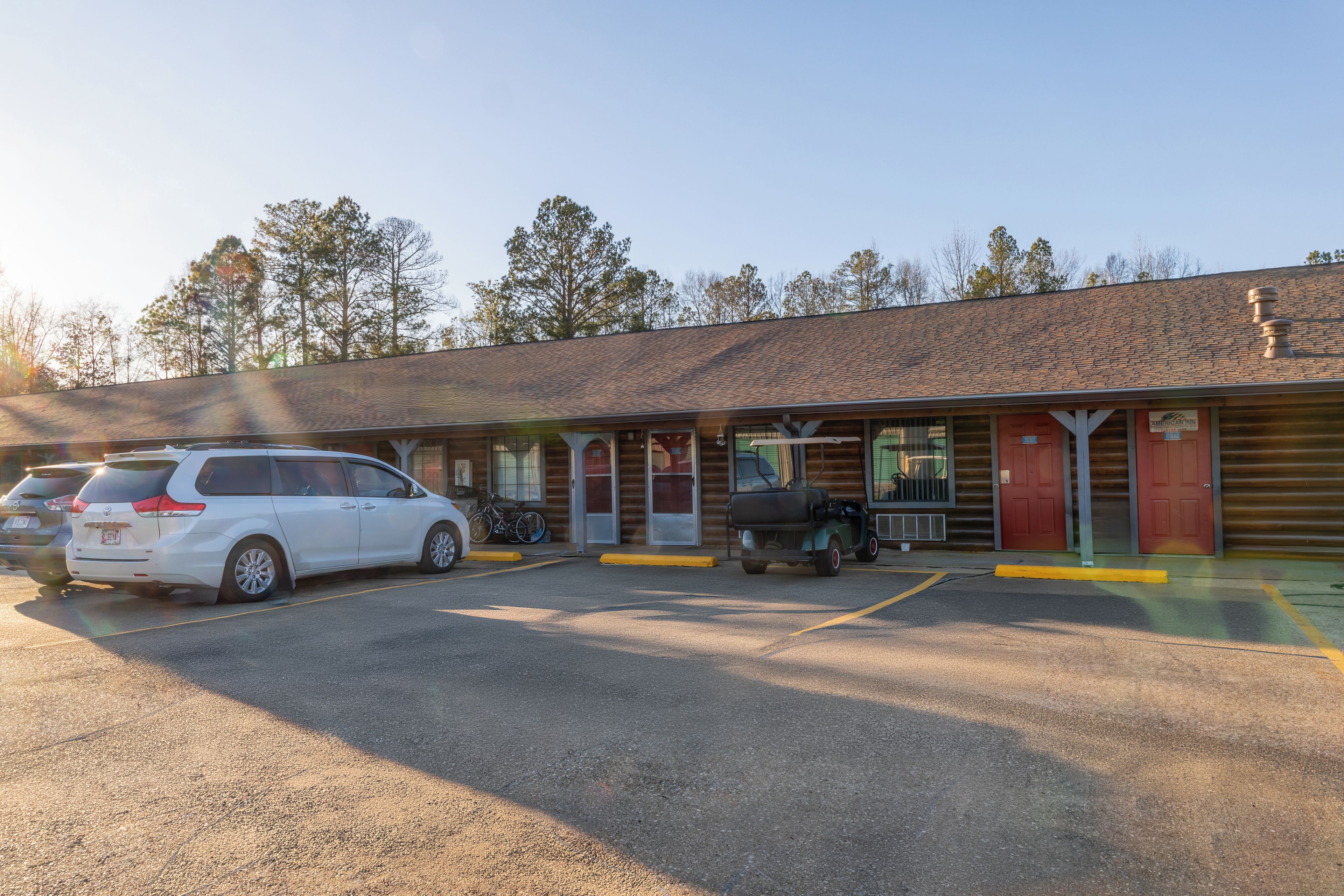 A motel with a parking lot, a covered outdoor seating area, and a building with a sloped roof.