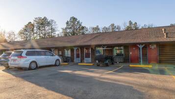 A motel with a parking lot, a covered outdoor seating area, and a building with a sloped roof.