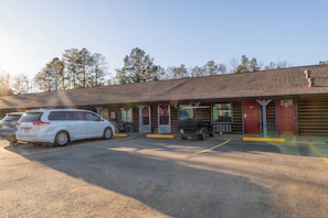 A motel with a parking lot, a covered outdoor seating area, and a building with a sloped roof.