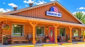 A wooden American Inn with a red door, large windows, and outdoor seating. - American Inn Motel by Capital O Camden AL (Camden)