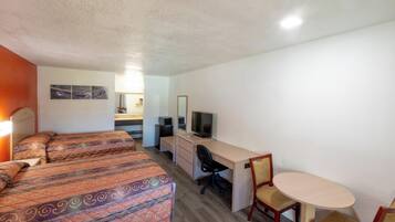 A hotel room with two beds, a desk, a chair, a television, and a small table.