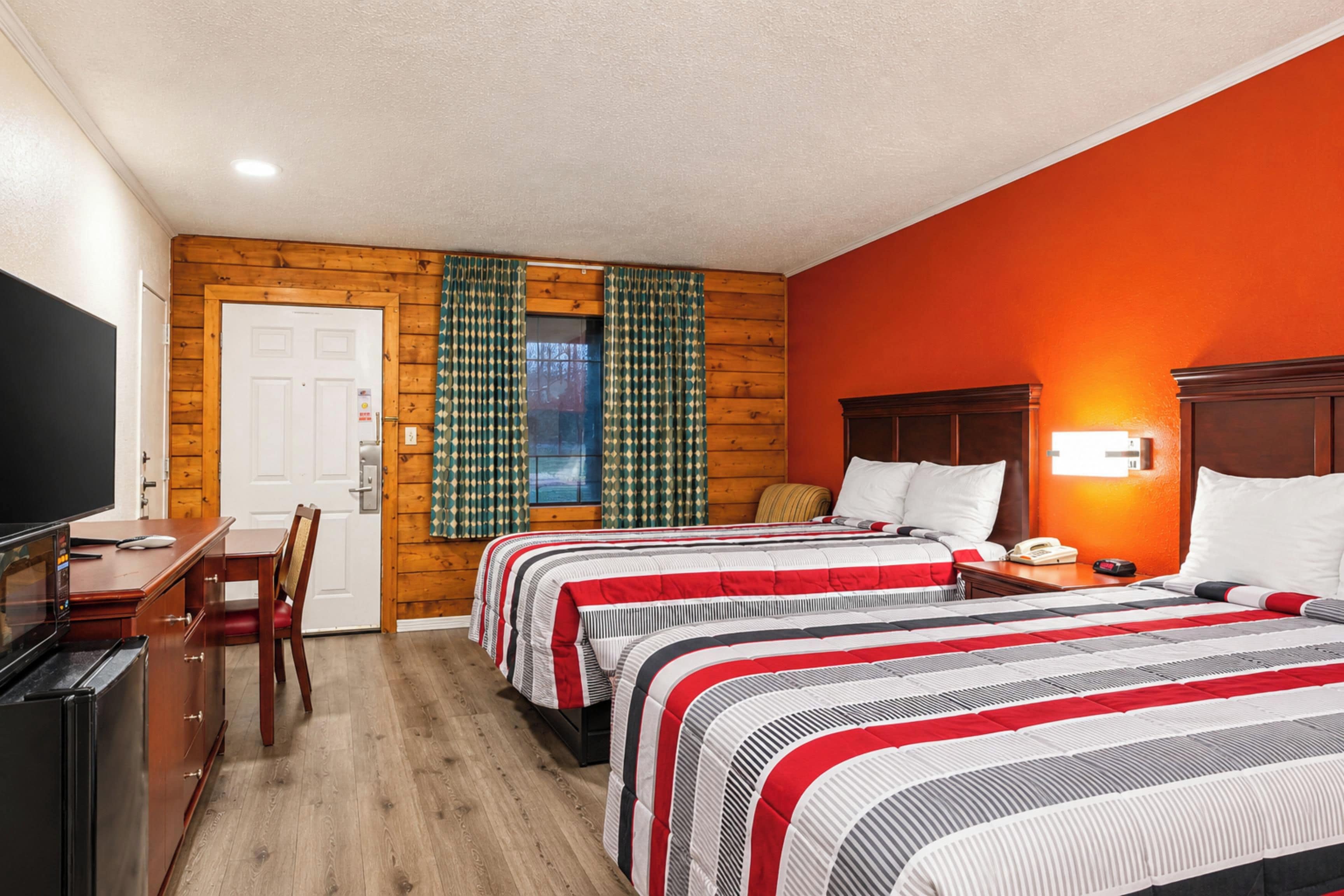 A hotel room with two beds, a desk with a TV, and a wooden wall.