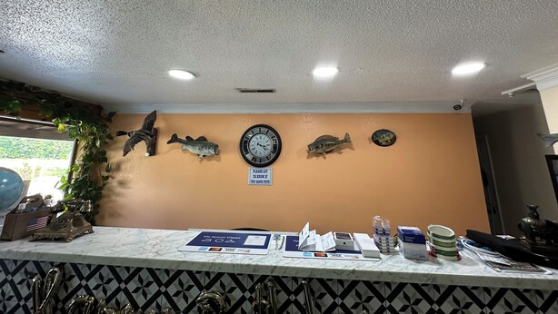 A reception area with a marble counter, a clock, and wall-mounted fish decorations. - American Inn Motel by Capital O Camden AL (Camden)