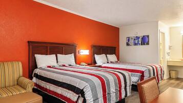 A hotel room with two beds, a wooden headboard, a striped sofa, and a small table.