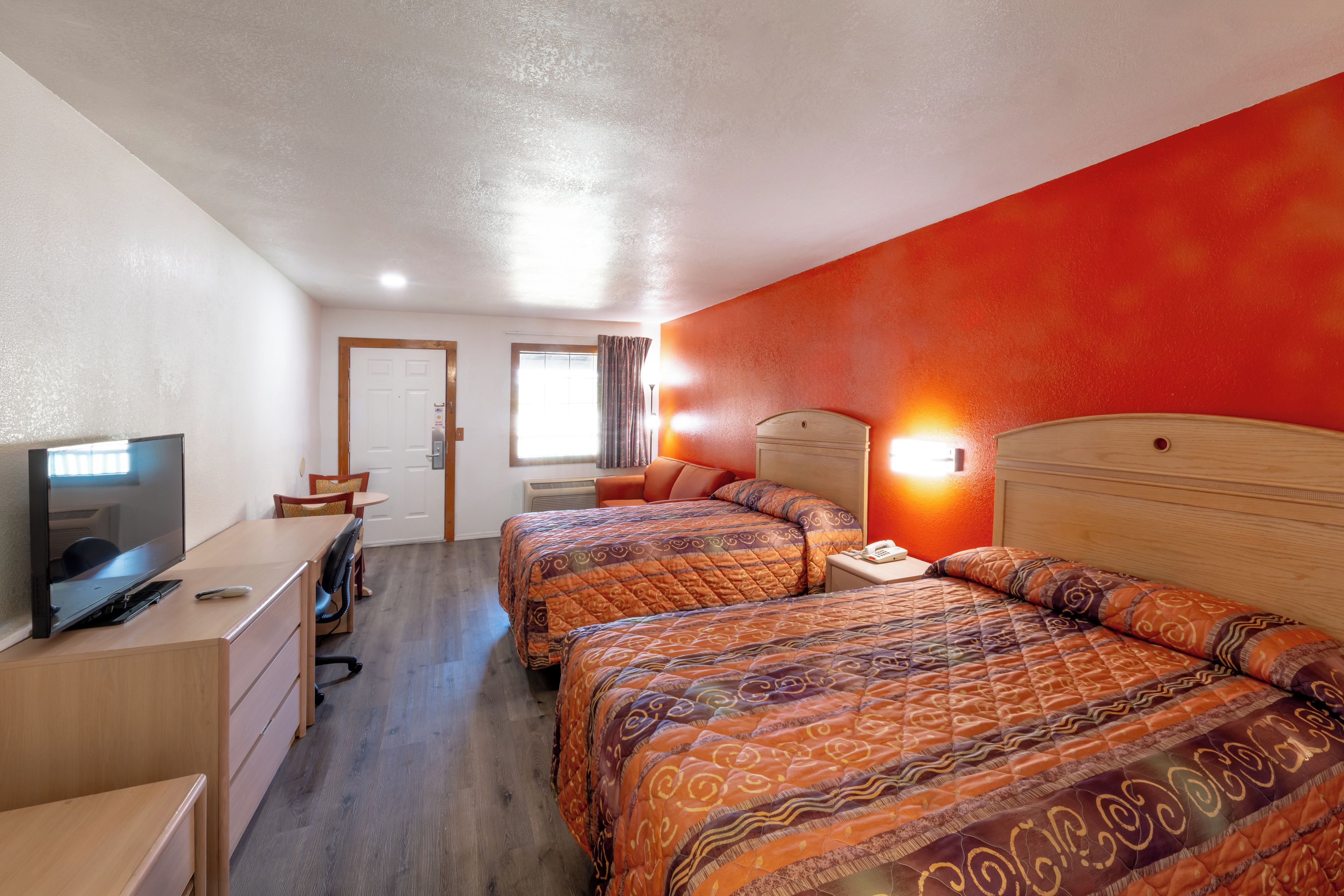 A hotel room with two beds, a desk with a television, and a door leading to another room.
