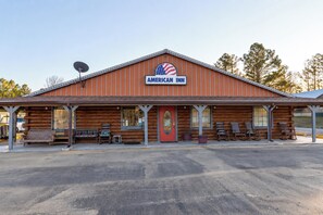 A two-story American Inn with a red exterior, a front porch with benches, and a satellite dish. - American Inn Motel by Capital O Camden AL (Camden)