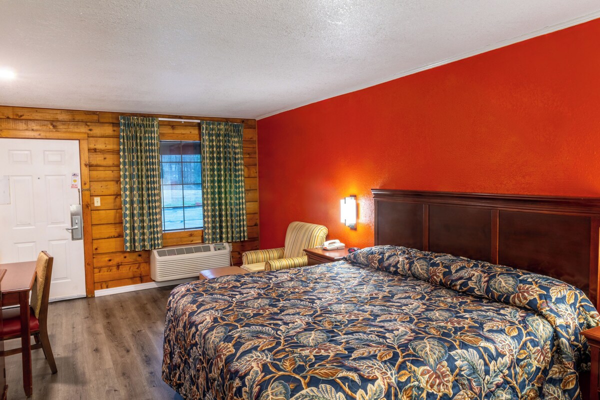 A room with a bed, a chair, a desk, and a window with curtains.