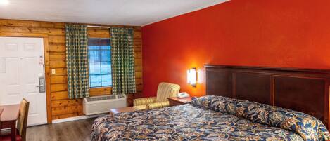 A room with a bed, a chair, a desk, and a window with curtains.