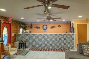 A lobby with a ceiling fan, a clock, fish wall art, a reception desk, and a door with an 'EXIT' sign. - American Inn Motel by Capital O Camden AL (Camden)
