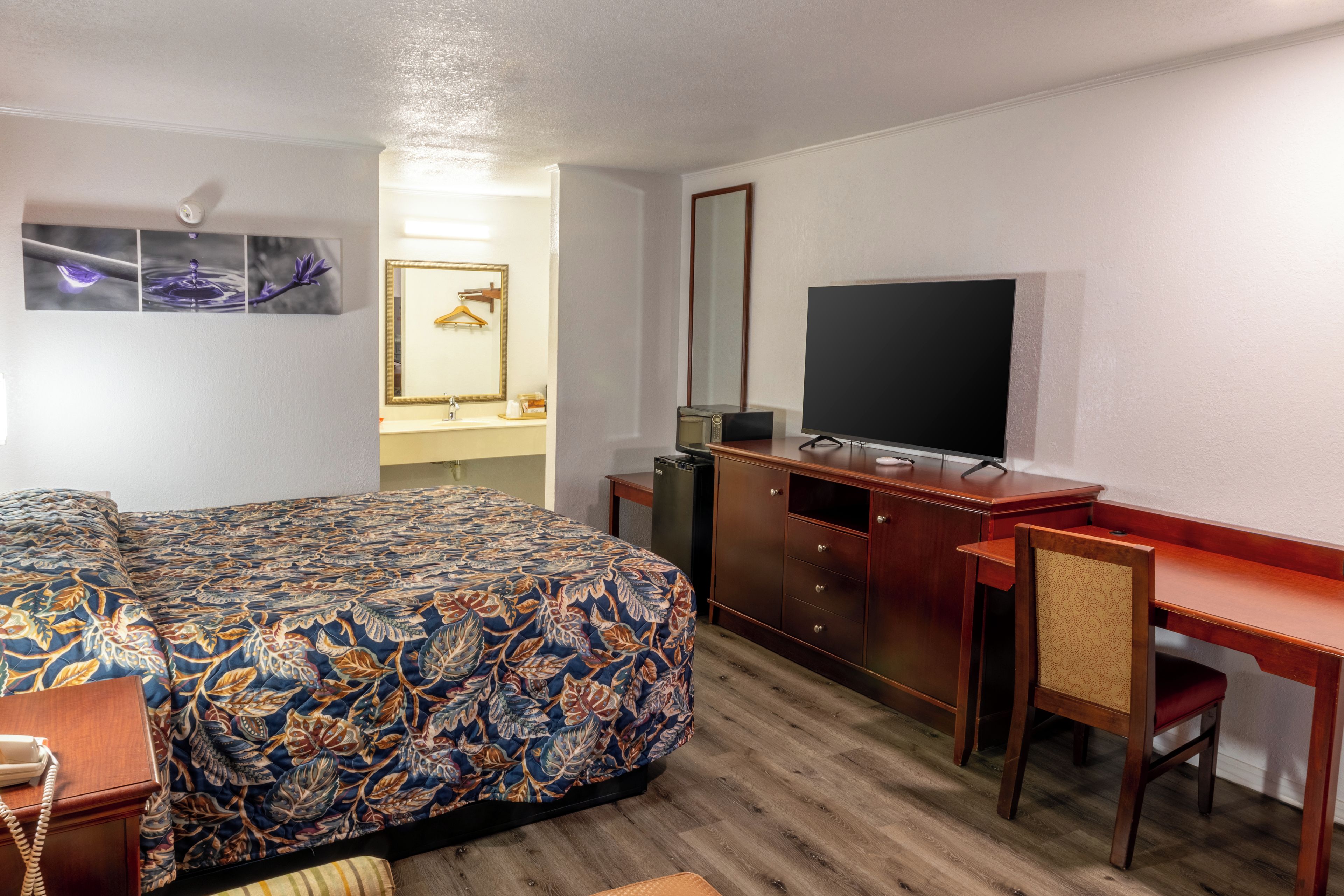 A hotel room with a bed, a desk, a television, a mirror, and a dresser.