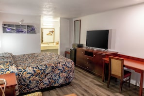 A hotel room with a bed, a desk, a television, a mirror, and a dresser.