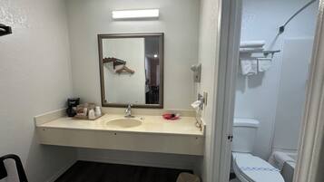 A bathroom with a white sink, a mirror, a hanging towel, a toilet, and a trash bin.