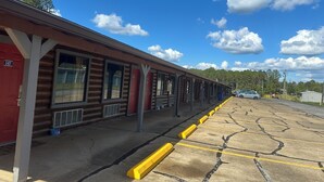 A row of log cabin-style rooms with large windows, a covered outdoor area, and a parking lot with yellow curbs. - American Inn Motel by Capital O Camden AL (Camden)
