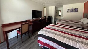 A hotel room with a desk, a television, a bed with striped bedding, a mirror, and a small artwork on the wall. - American Inn Motel by Capital O Camden AL (Camden)