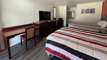 A hotel room with a desk, a television, a bed with striped bedding, a mirror, and a small artwork on the wall.