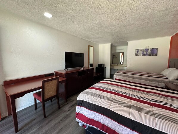 A hotel room with a desk, a television, a bed with striped bedding, a mirror, and a small artwork on the wall.