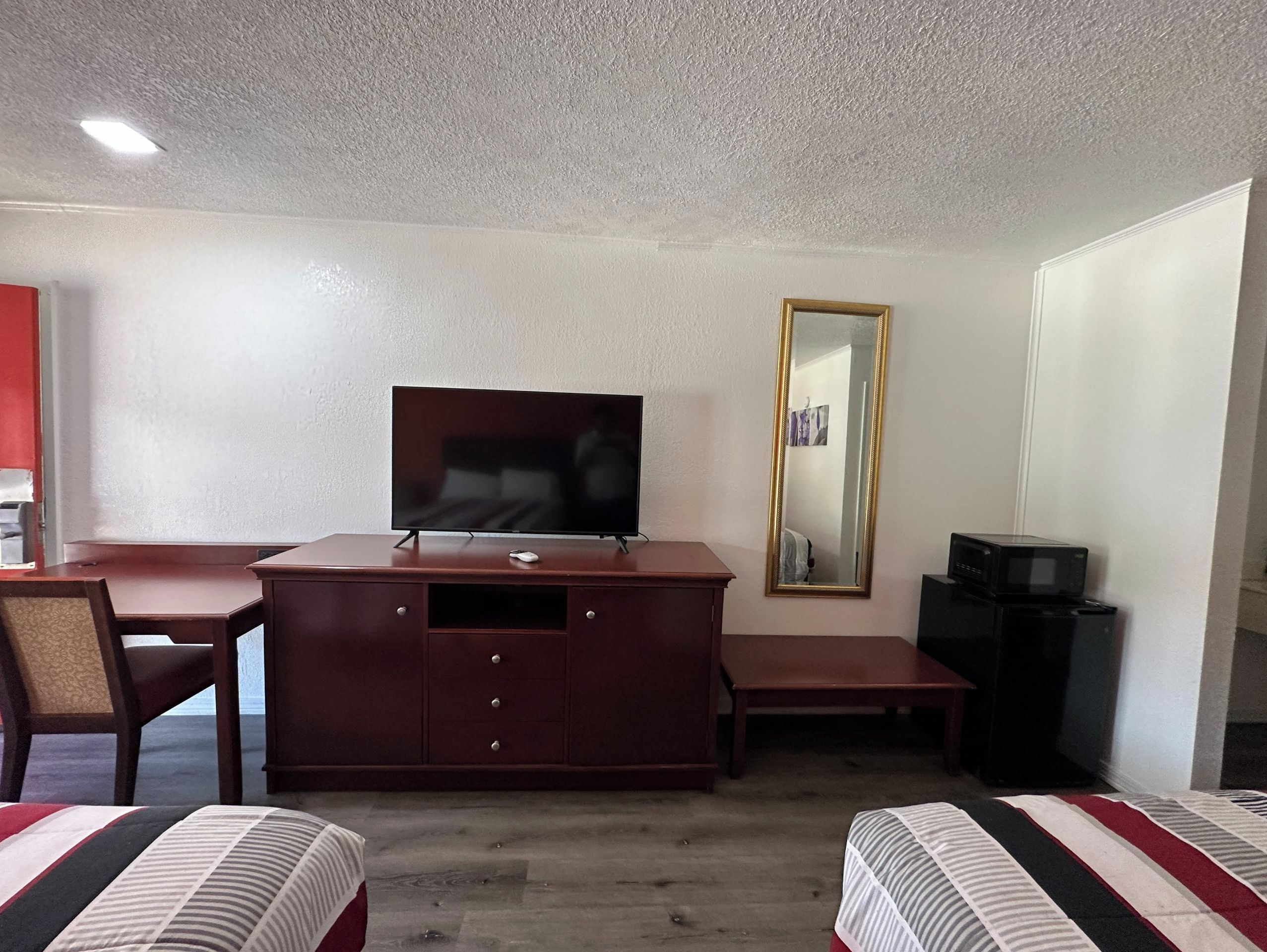 Una habitación de hotel con una televisión sobre un mueble de madera, un espejo, un escritorio y dos camas.